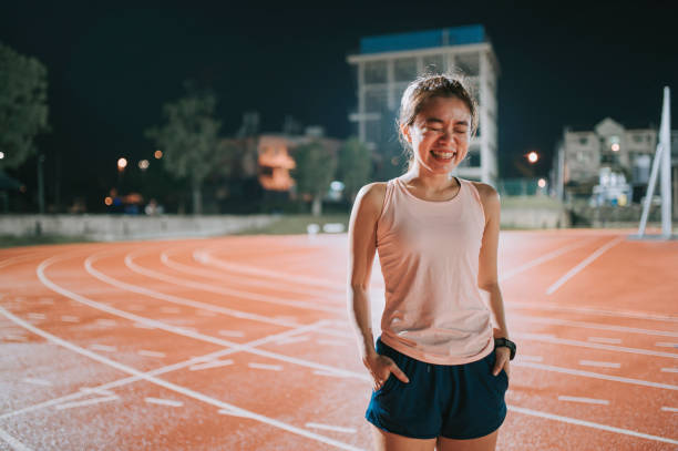 confidence and satisfied female athlete smiling with eyes closed standing on all-weather-track and field stadium at night - sports track track and field stadium sport night imagens e fotografias de stock