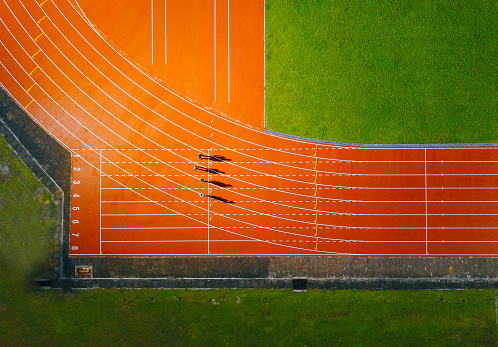 directamente por encima del punto de vista del dron atleta asiático chino masculino corriendo en la pista de los hombres lluvioso tarde por la noche en el estadio photo