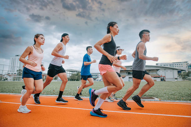 seitenansicht asiatisches chinesisches athletenteam läuft am bewölkten abend im leichtathletikstadion - mixed age stock-fotos und bilder