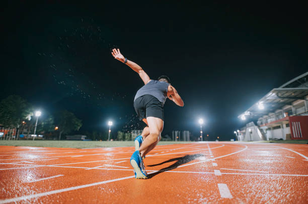 rear view aerodynamic asian chinese male athletes sprint running at track and run towards finishing line at track and field stadium track rainy night - sports track track and field stadium sport night imagens e fotografias de stock