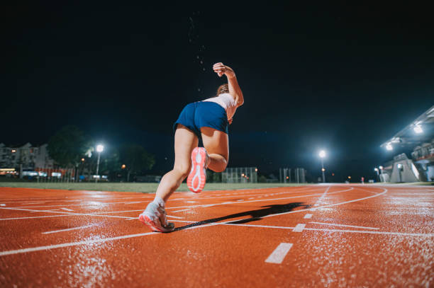 rear view aerodynamic asian chinese female athletes sprint running at track and run towards finishing line at track and field stadium track rainy night - sports track track and field stadium sport night imagens e fotografias de stock