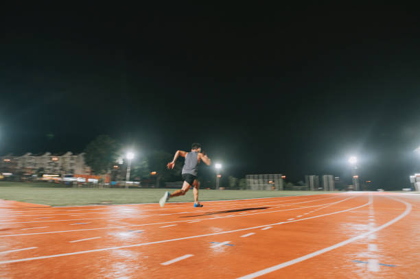 asian chinese male athletes sprint running at track and run towards finishing line at track and field stadium track rainy night - sports track track and field stadium sport night imagens e fotografias de stock