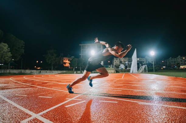 aerodynamic asian chinese male athletes sprint running at track and run towards finishing line at track and field stadium track rainy night - starting line sprinting track and field track event imagens e fotografias de stock