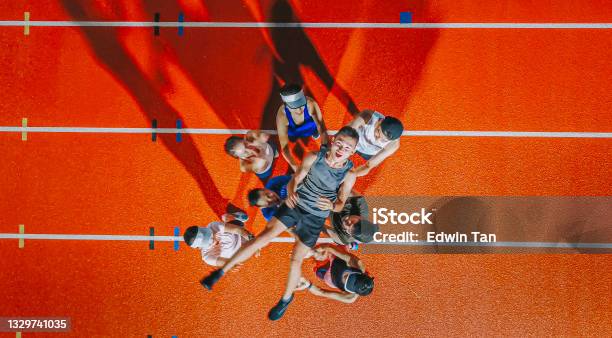 Directly Below Drone Point Of View Asian Chinese Athletes Cheering Throwing Lift Up Their Captain Winner Mid Air At Storm Cloud Late Evening In Stadium Stock Photo - Download Image Now