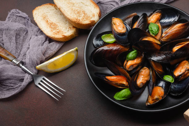 istock Seafood mussels and basil leaves in a black plate with bread slice, lemon, and fork on rusty background 1329745066