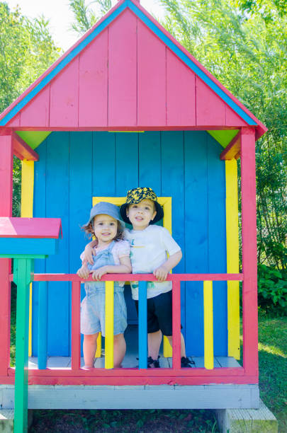 Little girl and boy and wooden toy house Little girl and boy on porch of colorful wooden toy house during summer day kids play house stock pictures, royalty-free photos & images