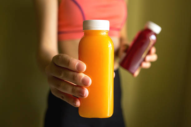 a female athlete holds bottles of freshly squeezed vegetable or fruit juice in her hands. the concept of a healthy lifestyle, a healthy body - freshly squeezed orange juice imagens e fotografias de stock