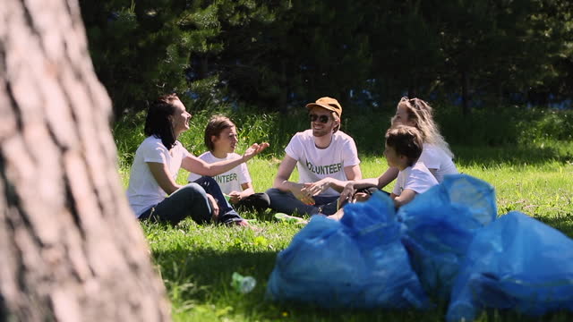 Young volunteers discussing environmental issues while sitting in green park on summer day spbi