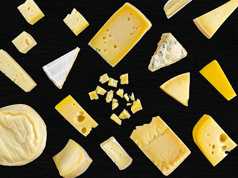 Group of Cheeses of different types on flat lay black background. Gorgonzola cheese, Italian Parmesan, Caciotta, French Brie, Swiss Cheese with holes