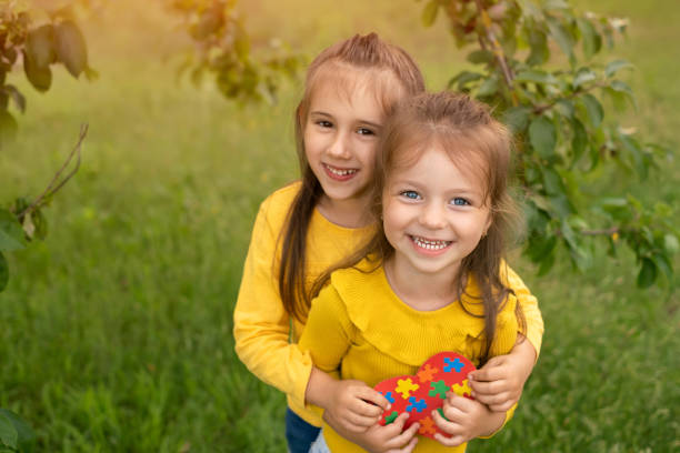 Two cute funny girls are holding a heart made of paper with puzzles Two cute funny girls are holding a heart made of paper with puzzles inside. World Autism Awareness Day. autism photos stock pictures, royalty-free photos & images