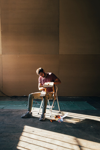 Young Caucasian man sitting on a chair in his workshop and making some furniture