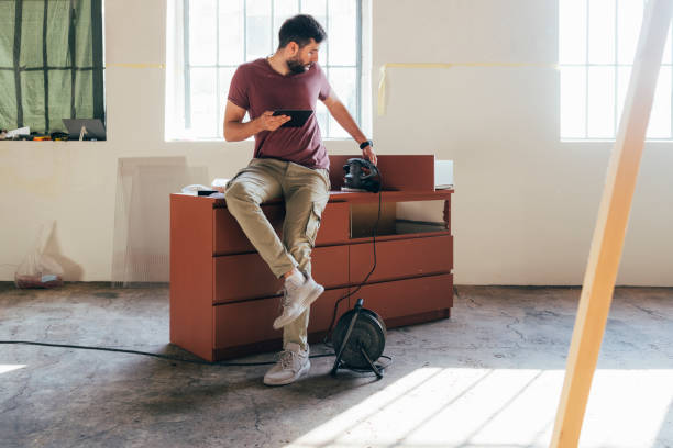 istock Handsome Young Man Sitting on a Chest of Drawers and Using a Tablet 1329755975