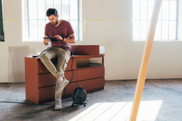 istock Handsome Young Man Sitting on a Chest of Drawers and Using a Tablet 1329755982