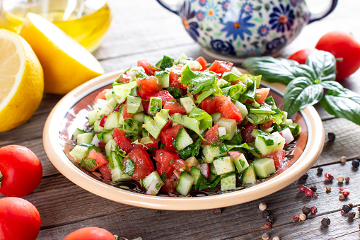 Delicious traditional Fattoush or bread salad with pita croutons, cucumber, tomato, lettuce and herbs on plate on wooden table, easy and healthy authentic recipe