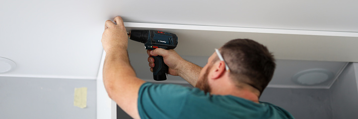 Carpenter assembles furniture at home using a screwdriver close-up. A man fixing a shelf to the ceiling