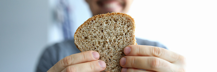 Close up happy guy holds piece whole grain bread. Healthy eating during self-isolation. Making homemade wholesome whole grain bread. Changing eating habits. Man bakes yeast-free bread