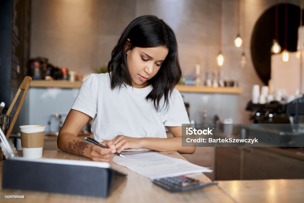 Female cafe owner signing papers calculating business expenses Tax Form Stock Photo