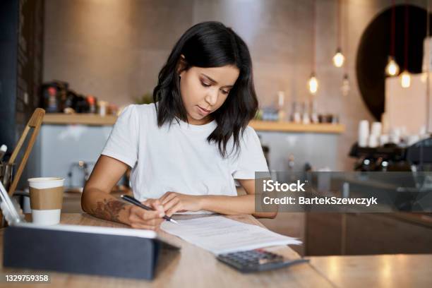 Female Cafe Owner Signing Papers Calculating Business Expenses Stock Photo - Download Image Now