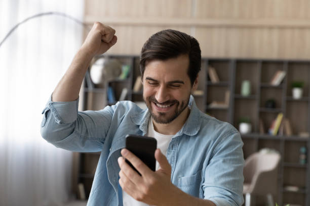 istock Overjoyed young man celebrating online success, holding cellphone. 1329762908