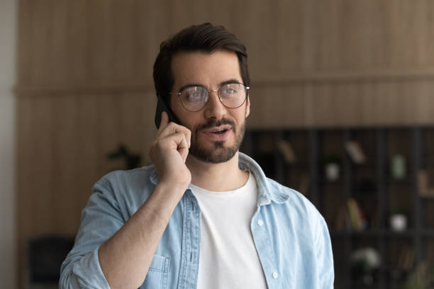 istock Happy young man in eyeglasses holding cellphone conversation. 1329762943