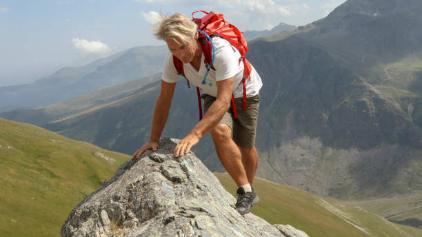 istock Mountaineer scrambles up sunny mountain ridge 1329764044