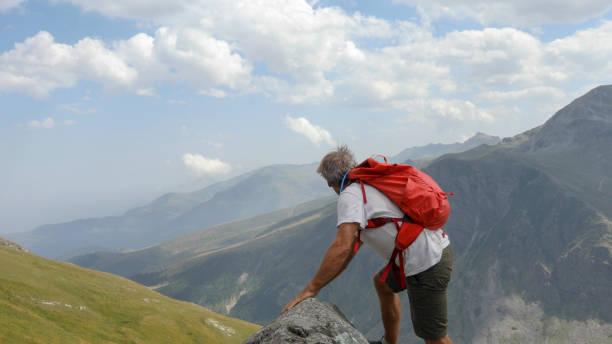 istock Mountaineer scrambles up sunny mountain ridge 1329764047