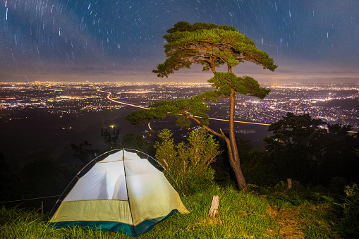 Camped on a mountain top overlooking city lights under a starry night sky.