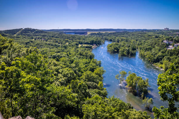 Sunny autumn afternoon at a lake in Springfield, Missouri, USA. Rocky edge to the lake surrounds the calm water. Sky is blue with a few white clouds.