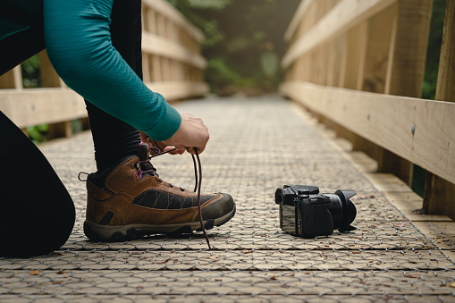 Woman tying hiking shoes with camera on the floor in outdoors.