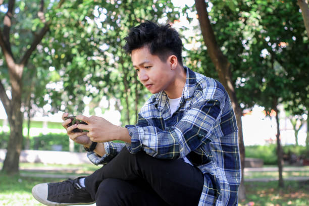istock Asian Young Men using a smartphone playing games in the park 1329784157