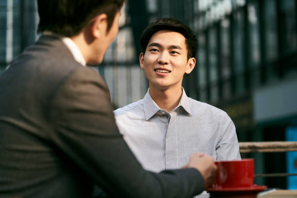 two asian business men talking in outdoor coffee shop stock photo