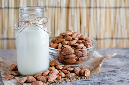 Closed up delicious homemade almond milk in glass bottle with some seed pile in glass bowl on grunge wooden background
