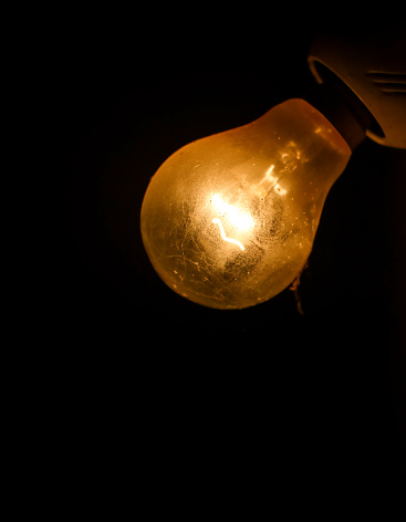 old and dusty incandescent light bulb filament glowing in a completely dark background with a hot orange light