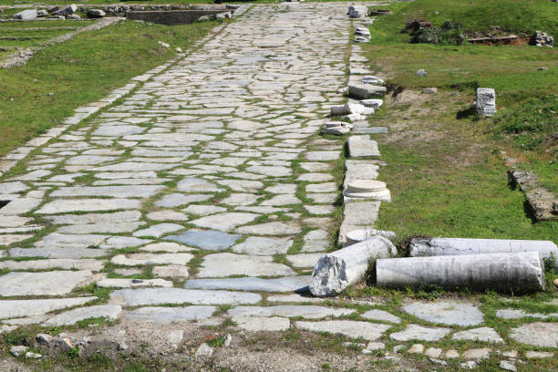 paisagem com uma estrada romana de pedra reta branca, ruínas de uma colunas quebradas e grama ao redor - paving stone cobblestone road old - fotografias e filmes do acervo