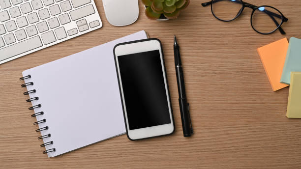 Mock up mobile phone, notebook, sticky notes and glasses on wooden desk.