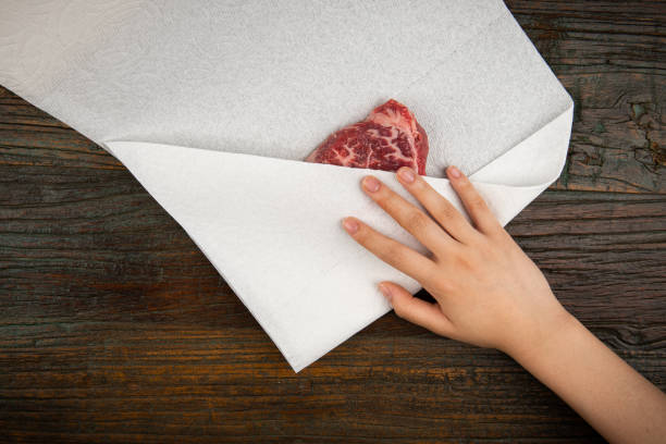 The raw meat is being drained with a kitchen towel