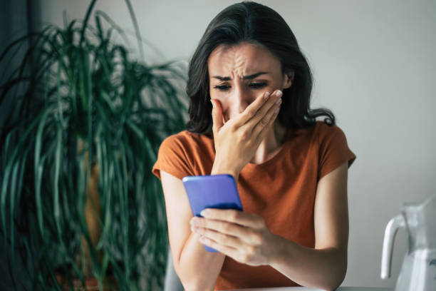 istock Sad, frustrated young brunette woman is crying with smartphone in hands while she sitting on the chair at apartment 1329809627