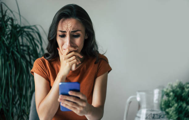 istock Sad, frustrated young brunette woman is crying with smartphone in hands while she sitting on the chair at apartment 1329809670