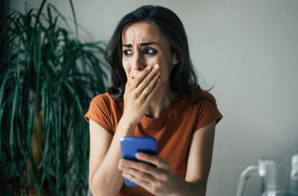 istock Sad, frustrated young brunette woman is crying with smartphone in hands while she sitting on the chair at apartment 1329809782