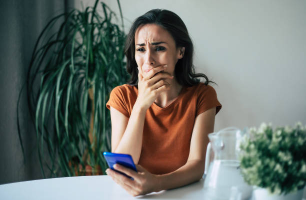 istock Sad, frustrated young brunette woman is crying with smartphone in hands while she sitting on the chair at apartment 1329809789
