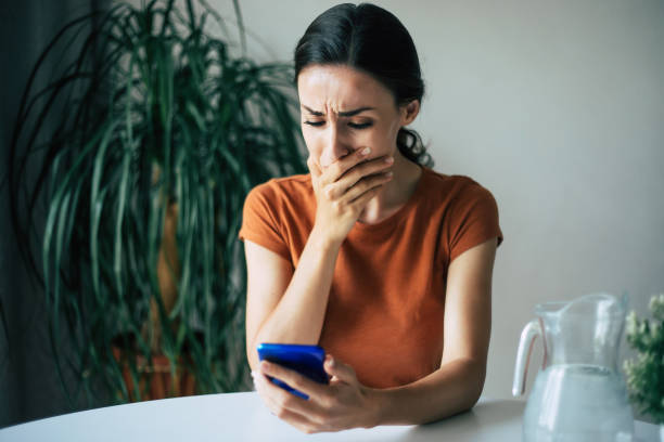 istock Sad, frustrated young brunette woman is crying with smartphone in hands while she sitting on the chair at apartment 1329809799