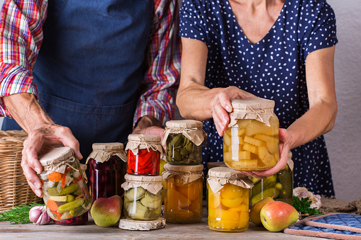Happy senior people holding in hands jars with homemade preserved and fermented food, pickled and marinated. Harvest preservation, family time