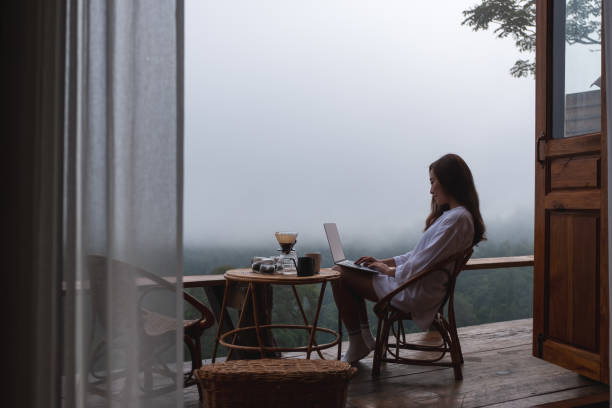 istock A young asian woman using and working on laptop computer while sitting on balcony with a beautiful nature view on foggy day 1329814687