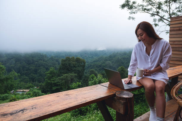 istock A young asian woman using and working on laptop computer while sitting on balcony with a beautiful nature view on foggy day 1329814731