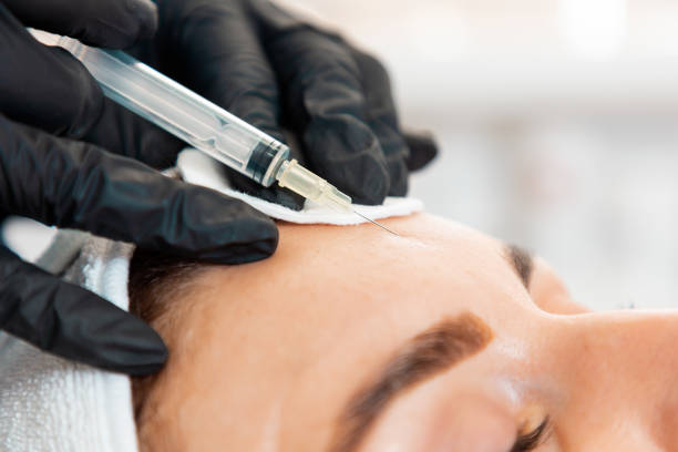 nahaufnahme des weiblichenkopfes, der im kosmetiksalon an die stirn spritzt. kosmetikerin in latexhandschuhen mit spritze injiziert ein medikament. konzept der plastischen chirurgie und des faceliftings - botox injection stock-fotos und bilder