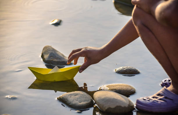 A teenager's hand launches a paper boat on a mountain river stock photo