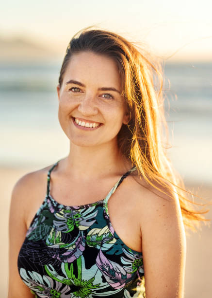 istock Smiling young woman standing on a beach at sunset 1329822646