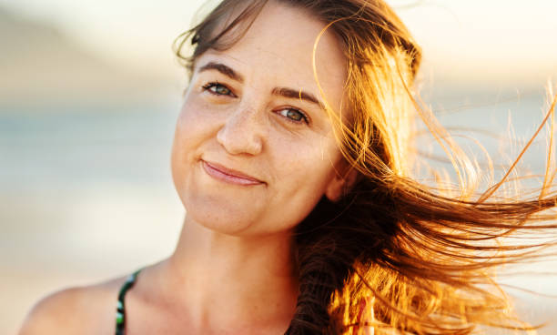 istock Smiling young woman standing on a breezy beach at sunset 1329822651