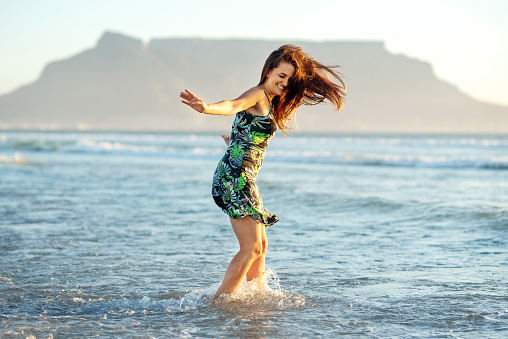 Carefree young woman laughing while splashing around in the ocean surf at the beach at sunset