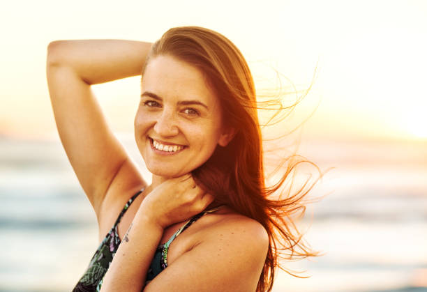istock Young woman smiling while standing on a breezy beach at dusk 1329822743